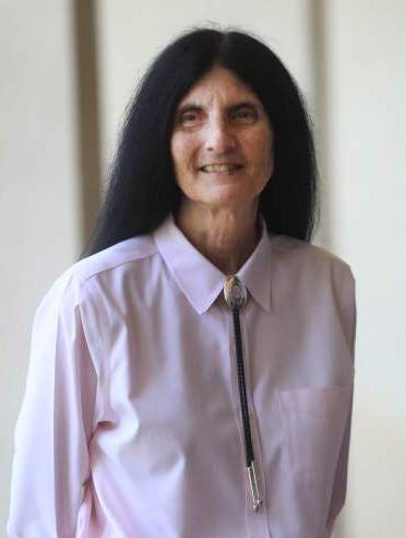 headshot of Dr. Brenda Flyswithhawks, smiling at the camera, has long black hair. 