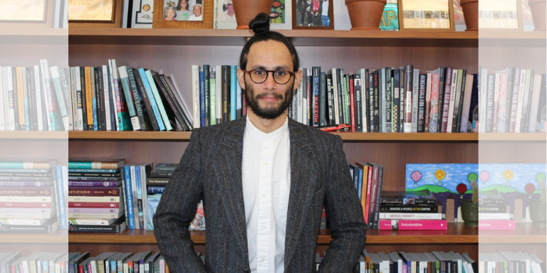 Dr. Uahikea Maile looking at the camera, standing in front of a bookshelf
