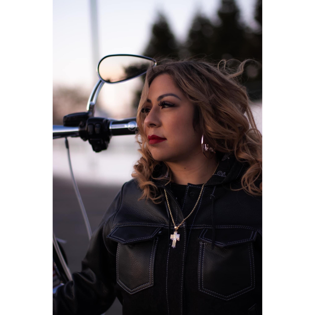 image of a person looking away from the camera. They have long wavy hair, red lips, and wearing black long sleeve. They are in front of a motorcycle mirror and handle bar.