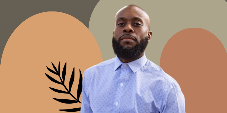 Image of a black man looking at the camera. He is bald and has a thick beard. Is wearing a Kentucky corn-blue button up shirt. Background has neutral brown, orange, and green.