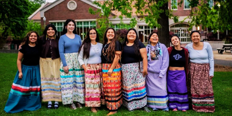 group of nine people with ribbon skirts facing the camera and smiling.