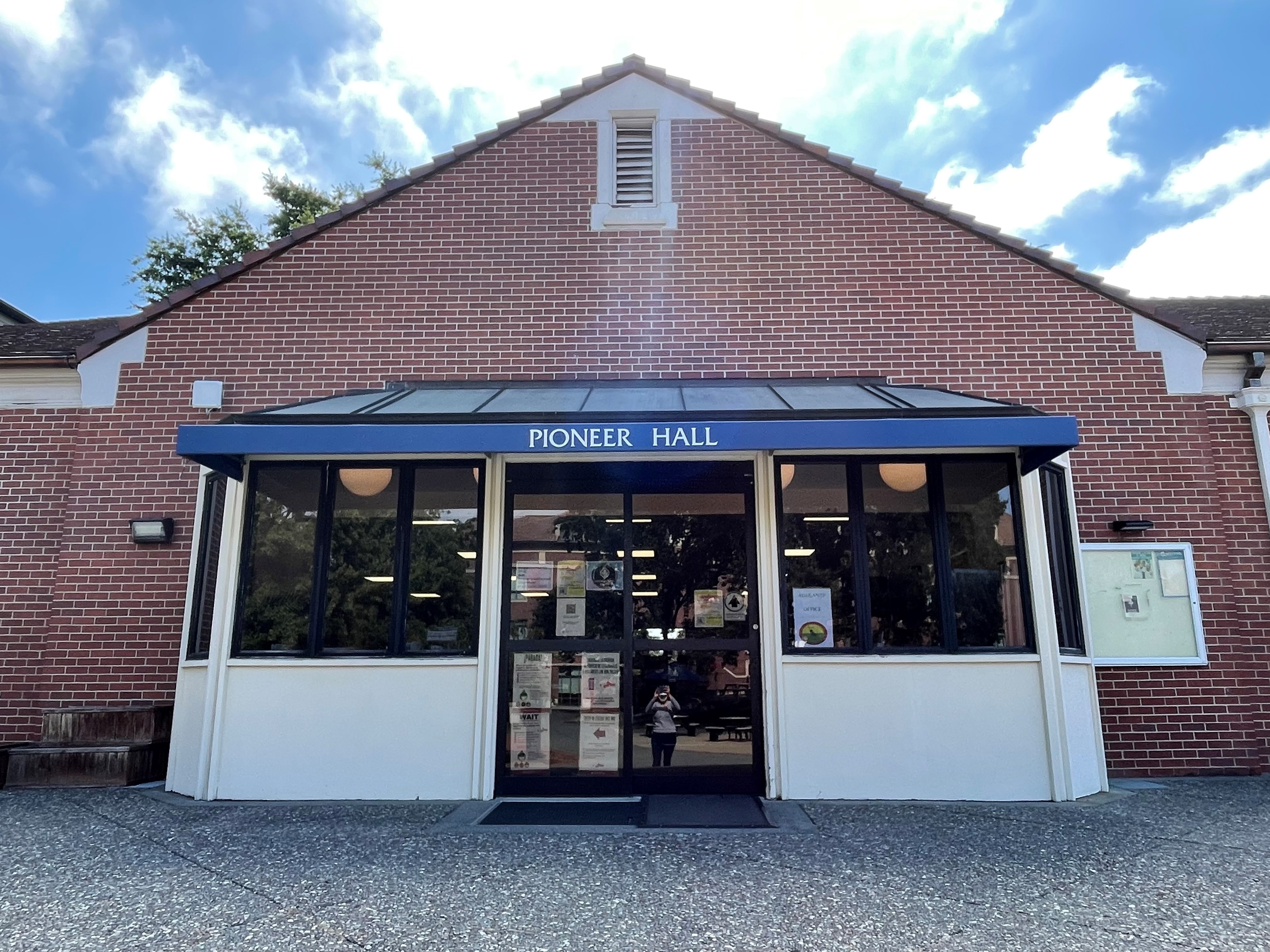 facade of a one story brick building that have the words "pioneer hall" written on a blue awning. 