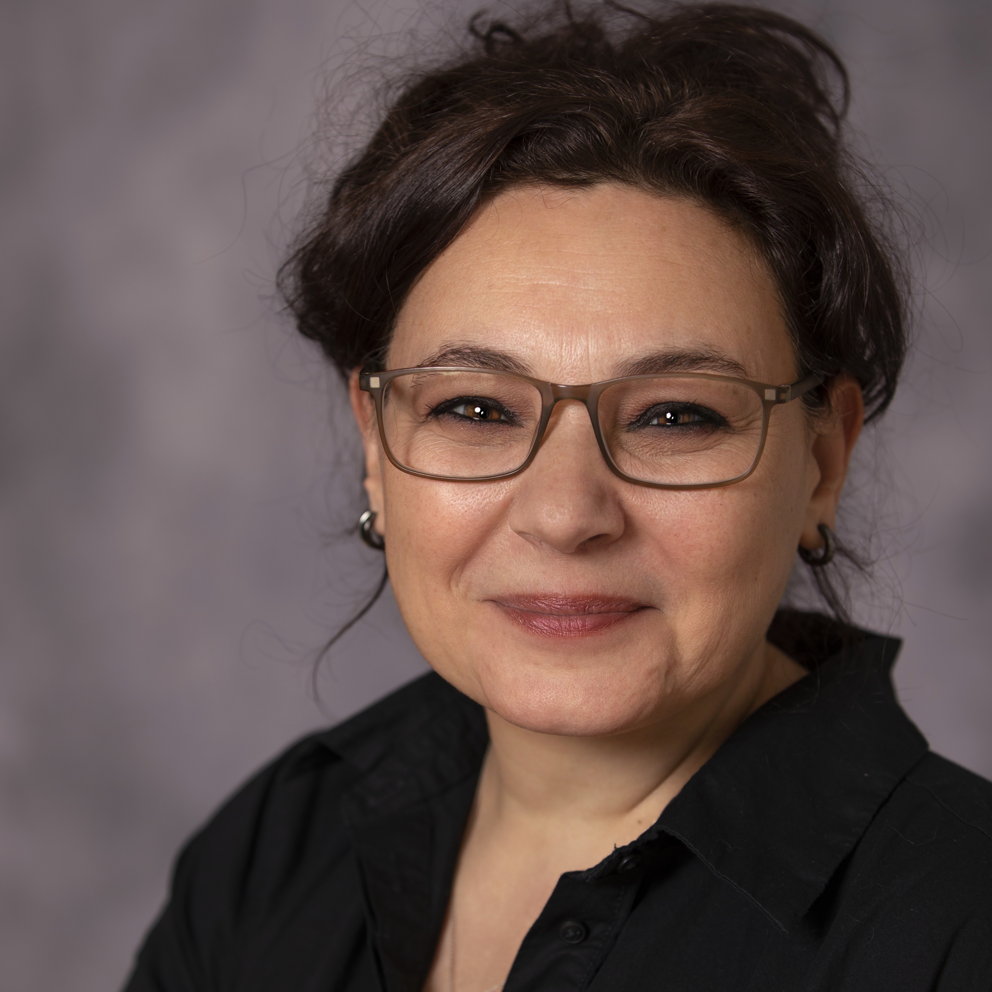 Head shot of Dr. Purnur Ozbirinci. She is wearing glasses and smiling at the camera. Her hair is in an up-do and she is wearing short earrings and a black blouse. 