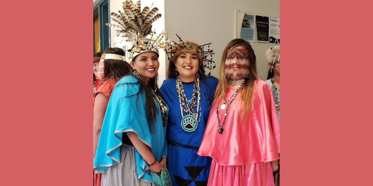 three people smiling at the camera wearing traditional women's ribbon skirts. 