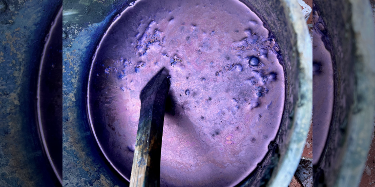 Closeup image of a dye vat with deep metallic purple dye in a large pot