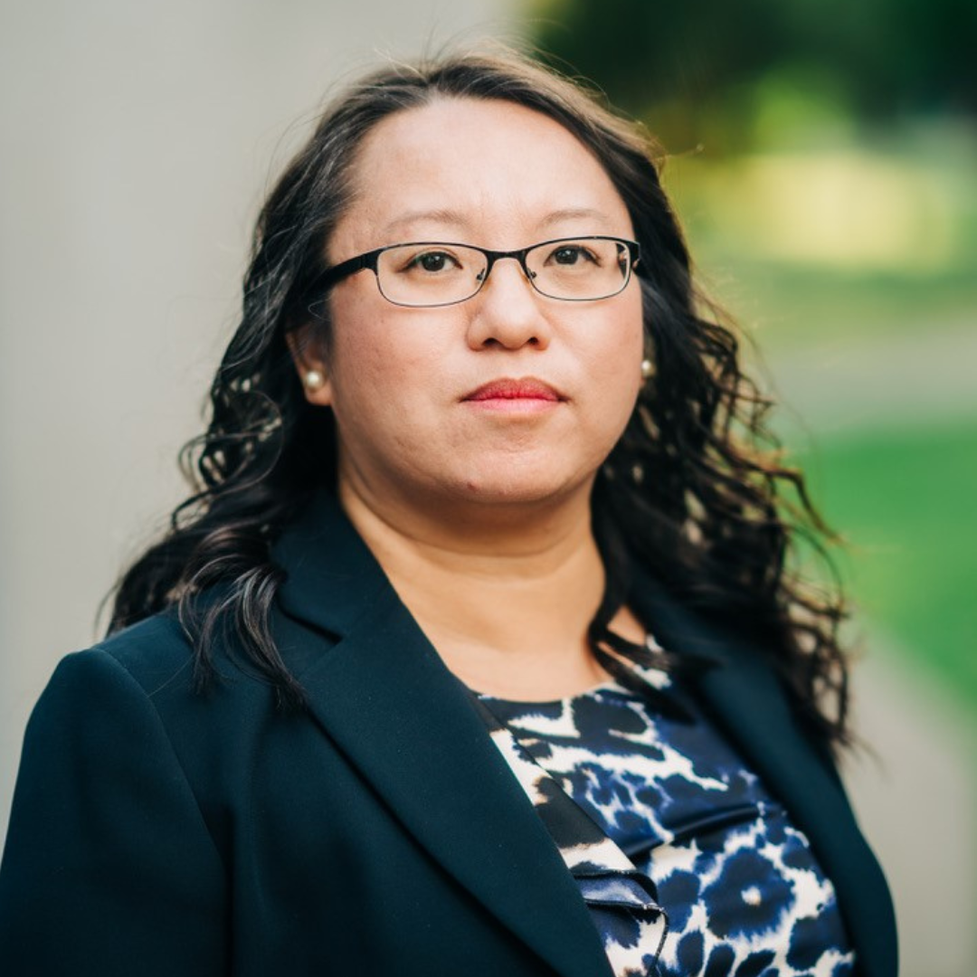 picture of Jerry thao looking at the camera. She has wavy hair, glasses, and a blue blazer
